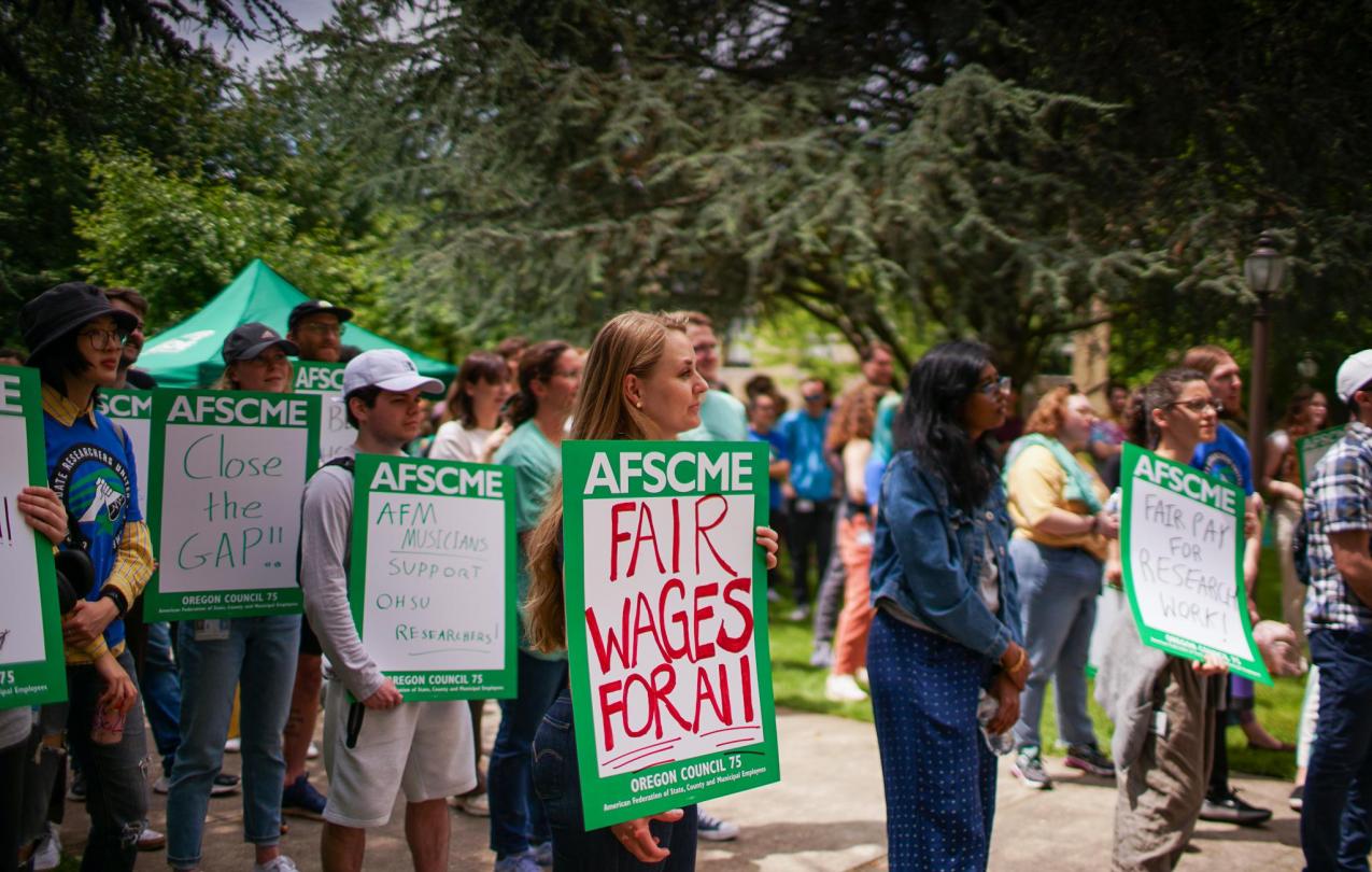 Group of research workers dressed in green, holding signs at a rally in front of OHSU